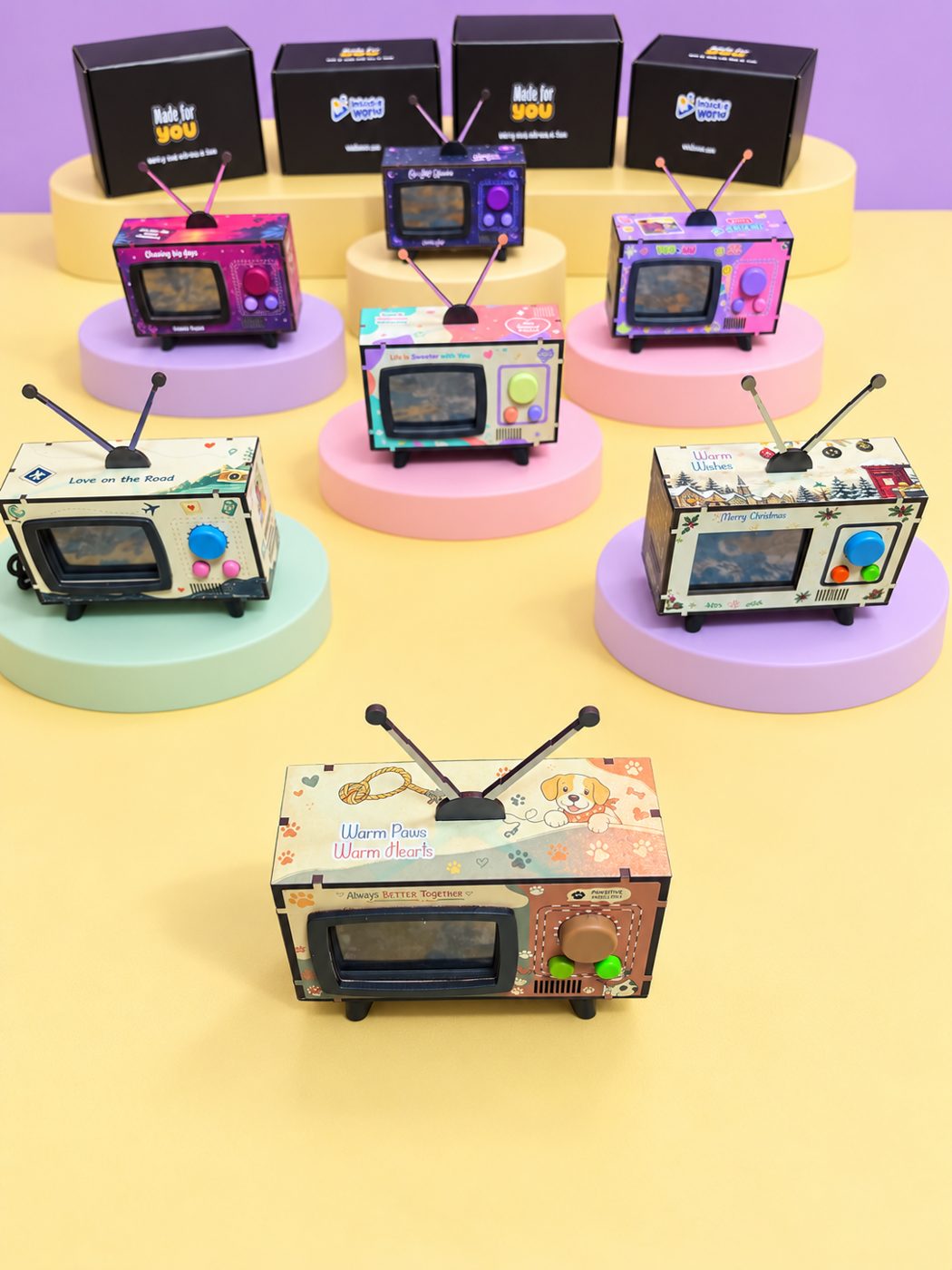 Mini TVs in different designs displayed on pastel pedestals with their gift boxes